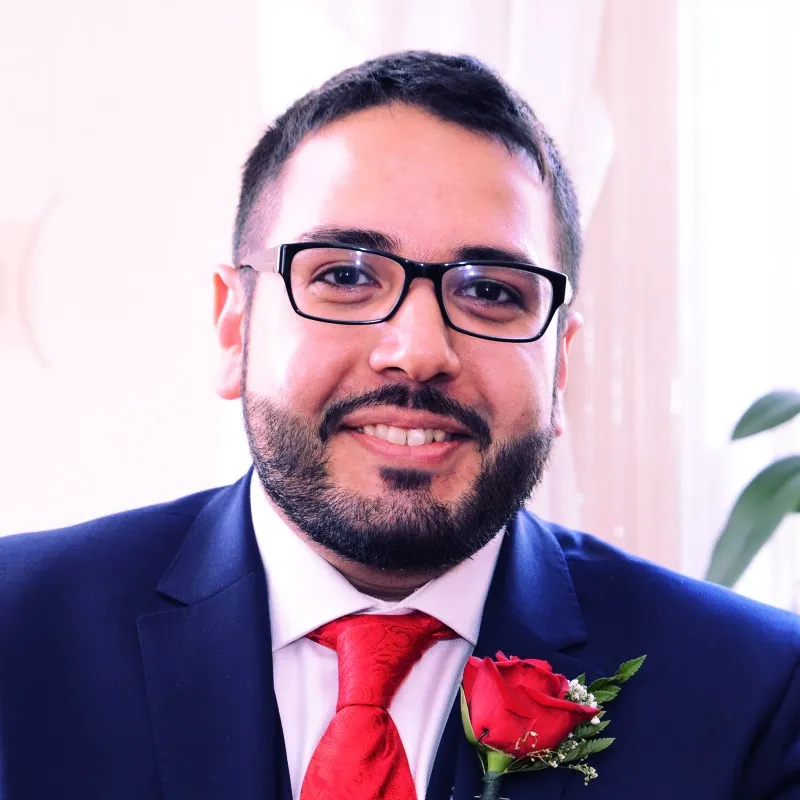 Portrait of a smiling bearded man in glasses, a navy suit, red tie and red rose buttonhole.