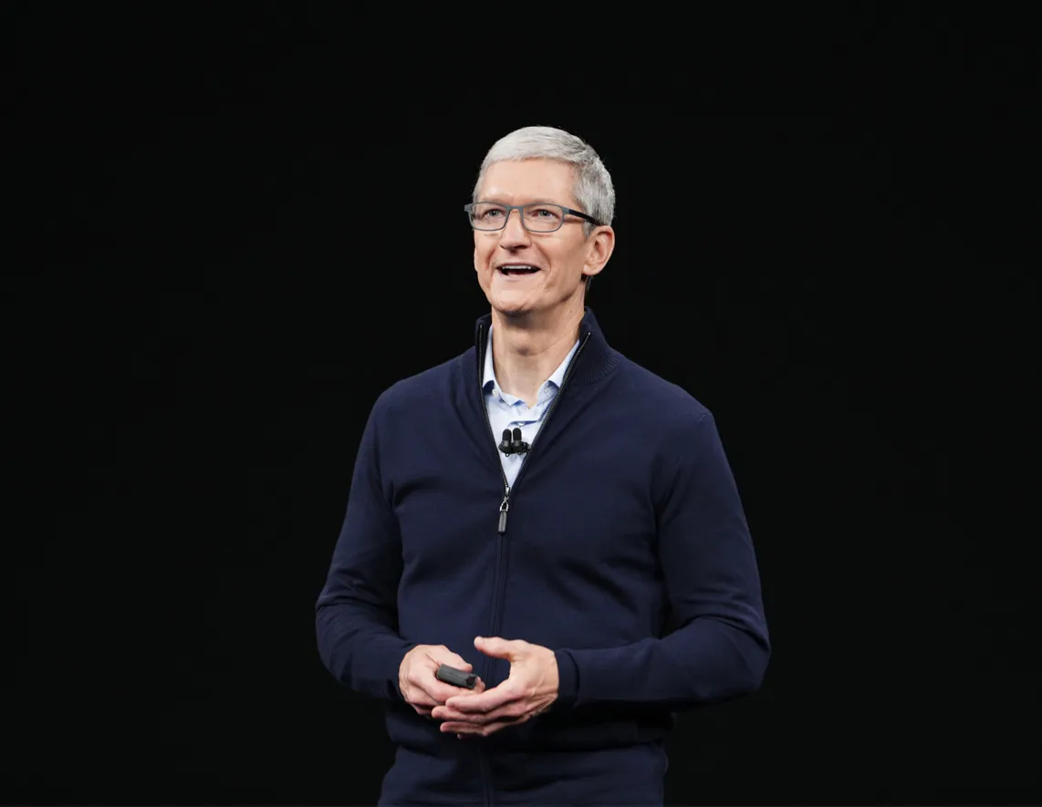 Portrait of a smiling man with grey hair and glasses in a navy zip-up top against a black background.