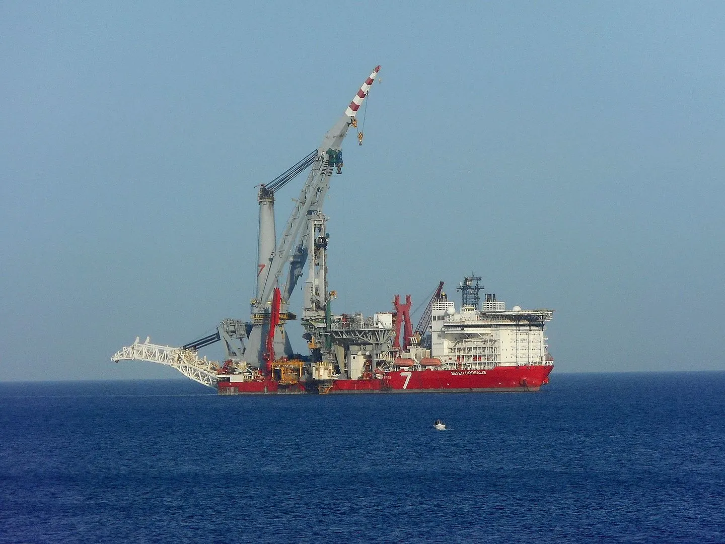 Red-hulled vessel 'Seven Borealis' with a tall crane, at sea under a clear sky
