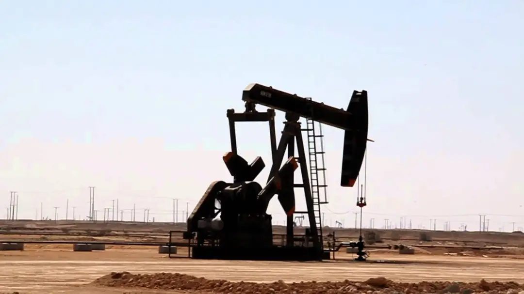 Pumpjack oil well in a flat, dry desert landscape under a pale sky
